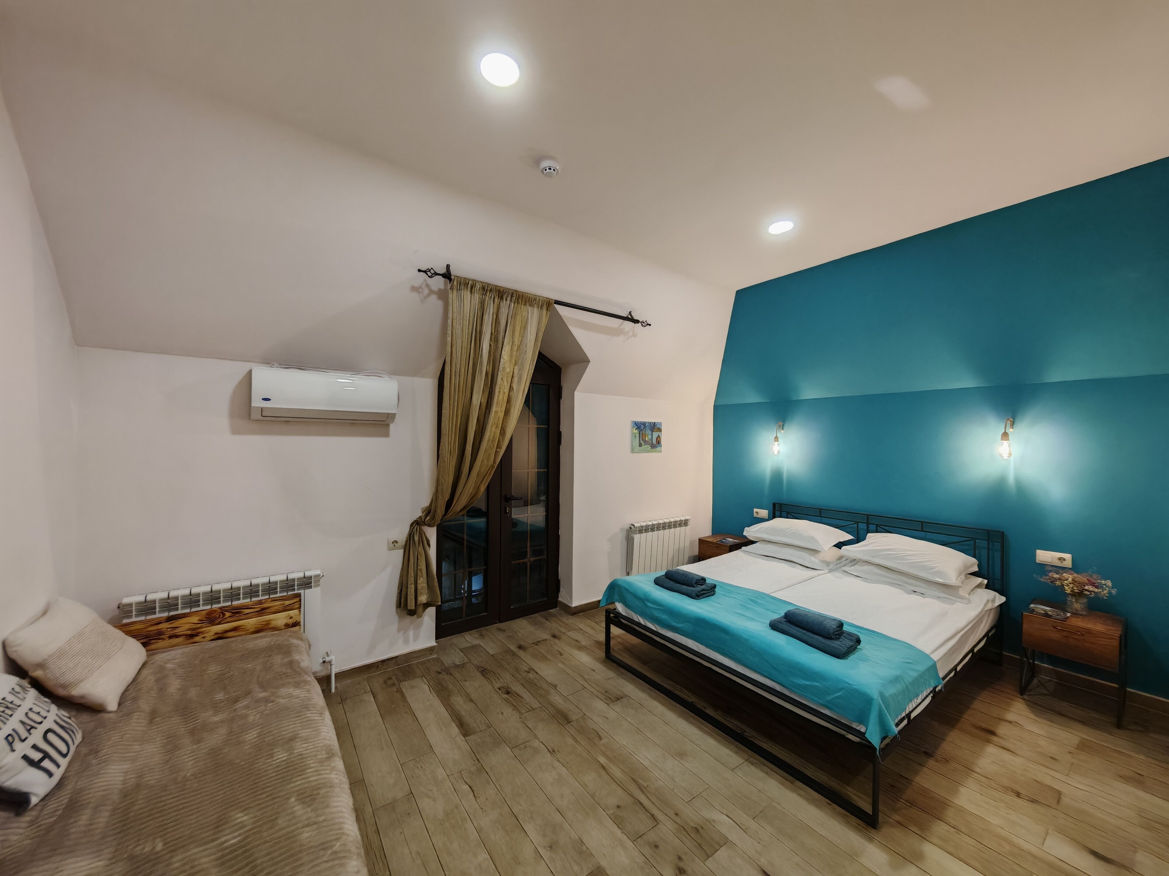 Un dormitorio con cama, sofá, ventana con cortinas, aire acondicionado y lámpara de pared.
