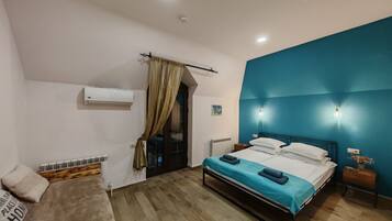 Un dormitorio con cama, sofá, ventana con cortinas, aire acondicionado y lámpara de pared.