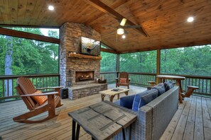 A wooden deck with a stone fireplace, seating, and a view of the forest. - Rohring Retreat - Bask in comfort on the deck and play games in the game room! (Mineral Bluff)