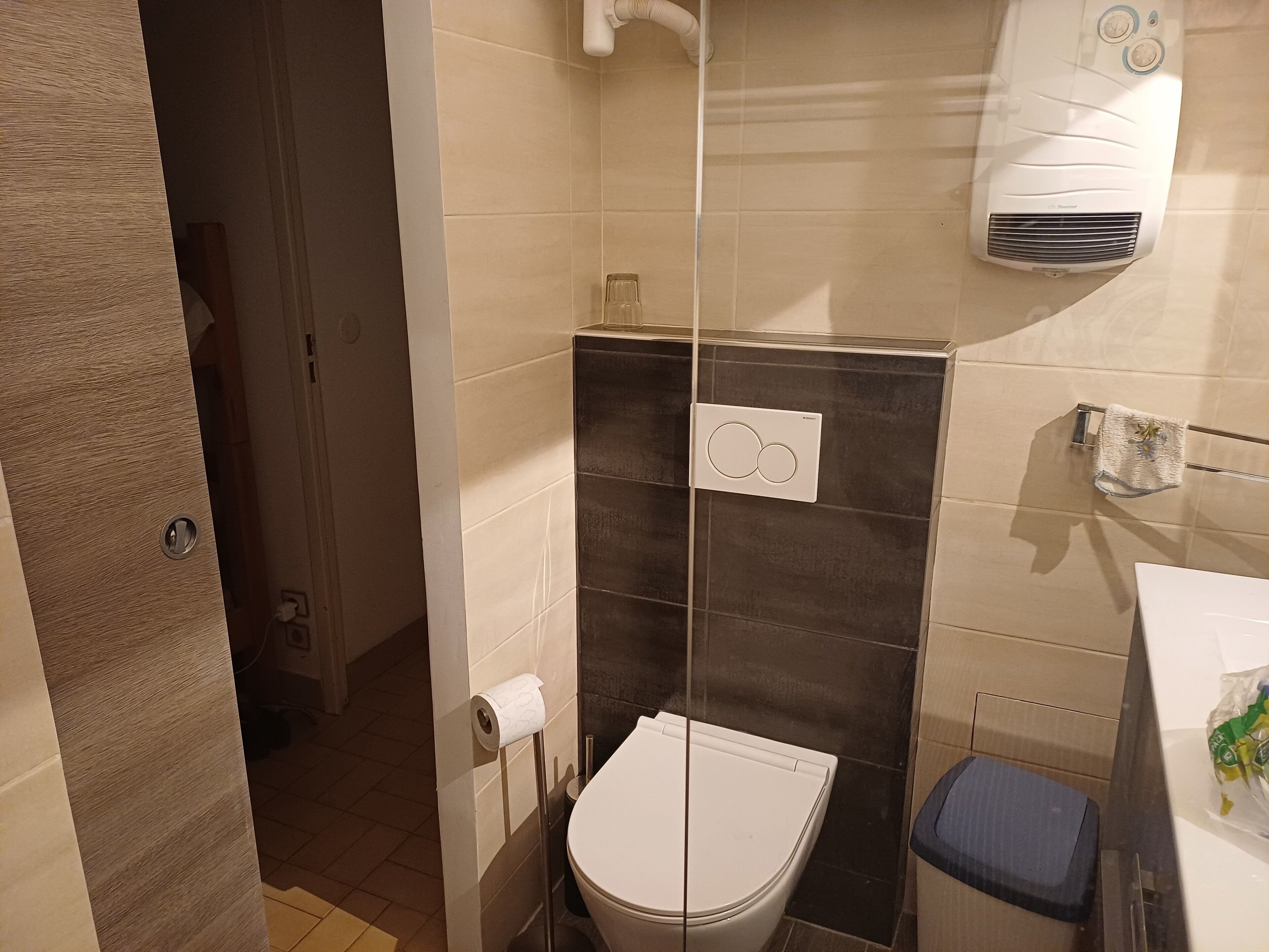 A bathroom with a toilet, a towel rack with a towel, a shower area, and a wall-mounted air conditioner.