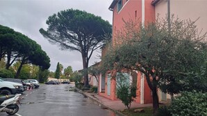 Un parcheggio con auto e una motocicletta, un edificio rosso con un grande albero di fronte e un cielo sereno.