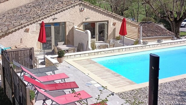 Zona de piscina con piscina, sombrillas rojas y vistas a un paisaje montañoso.