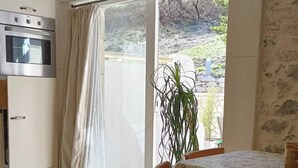 Una cocina con horno, una mesa de comedor con sillas y vistas a un espacio exterior por una puerta de vidrio.