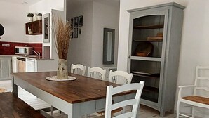 Un comedor con mesa de madera y sillas blancas, un armario blanco y una estantería con objetos decorativos.
