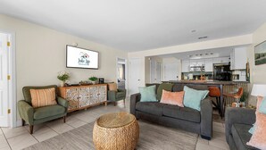 A modern living room with a sofa, a coffee table, and a kitchen in the background. - Table Rock Lake Views | Pool Steps from Patio | 2 Private Suites (Kimberling City)