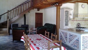Een eetruimte met een tafel voor vier personen, een open haard, een trap en een keuken met een gasfornuis.