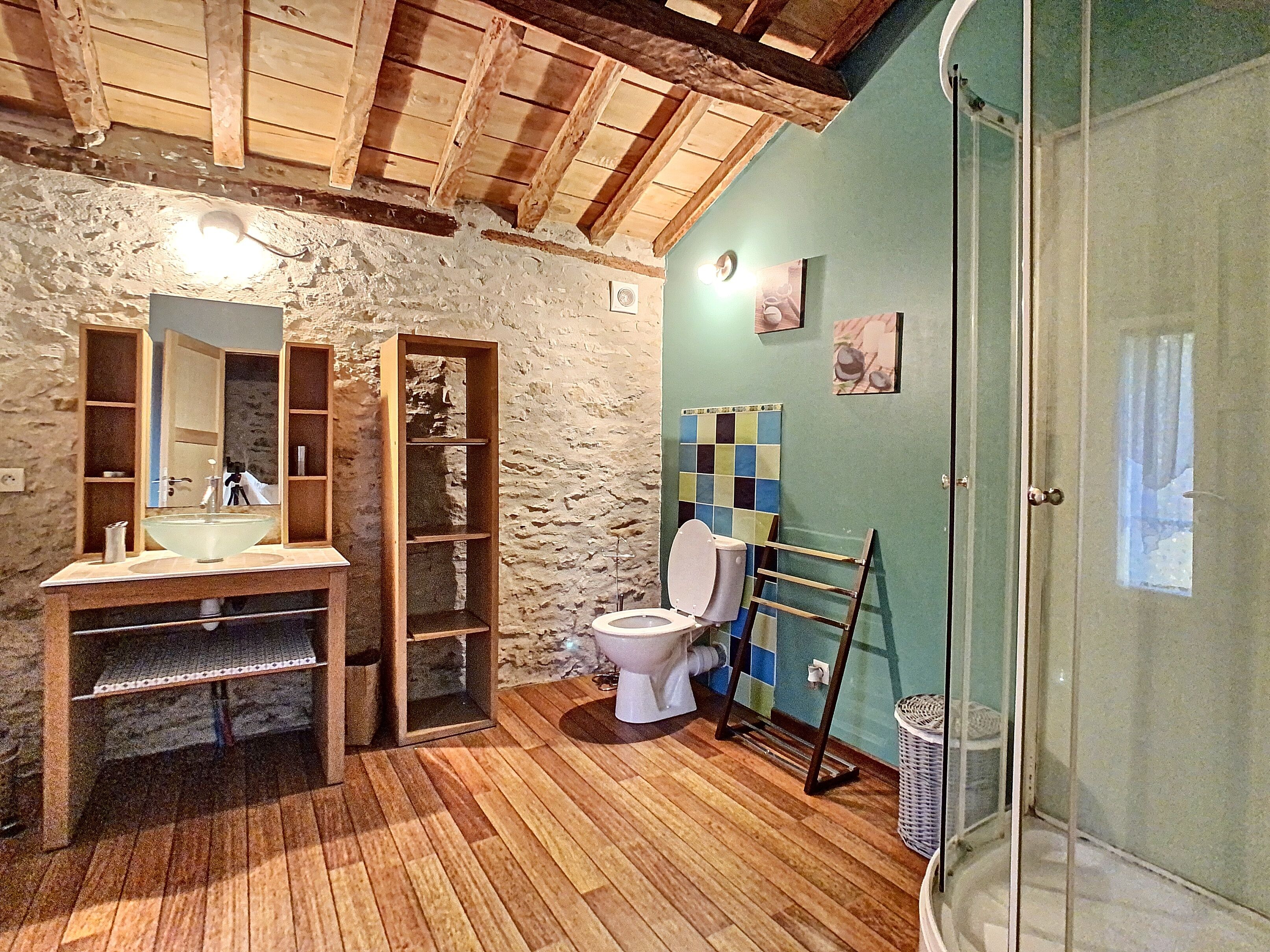 Een rustieke badkamer met een houten wastafelmeubel, een grote spiegel, een toilet en een douchehoek.