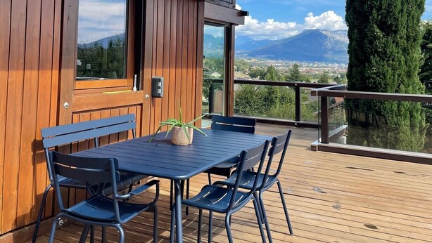 A wooden cabin with a deck, a table with chairs, and a view of mountains. - Exceptional mountain view, heated swimming pool, 10 minutes from Lake Annecy (sillingy)