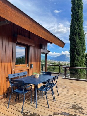 A wooden cabin with a deck, a table with chairs, and a view of mountains.