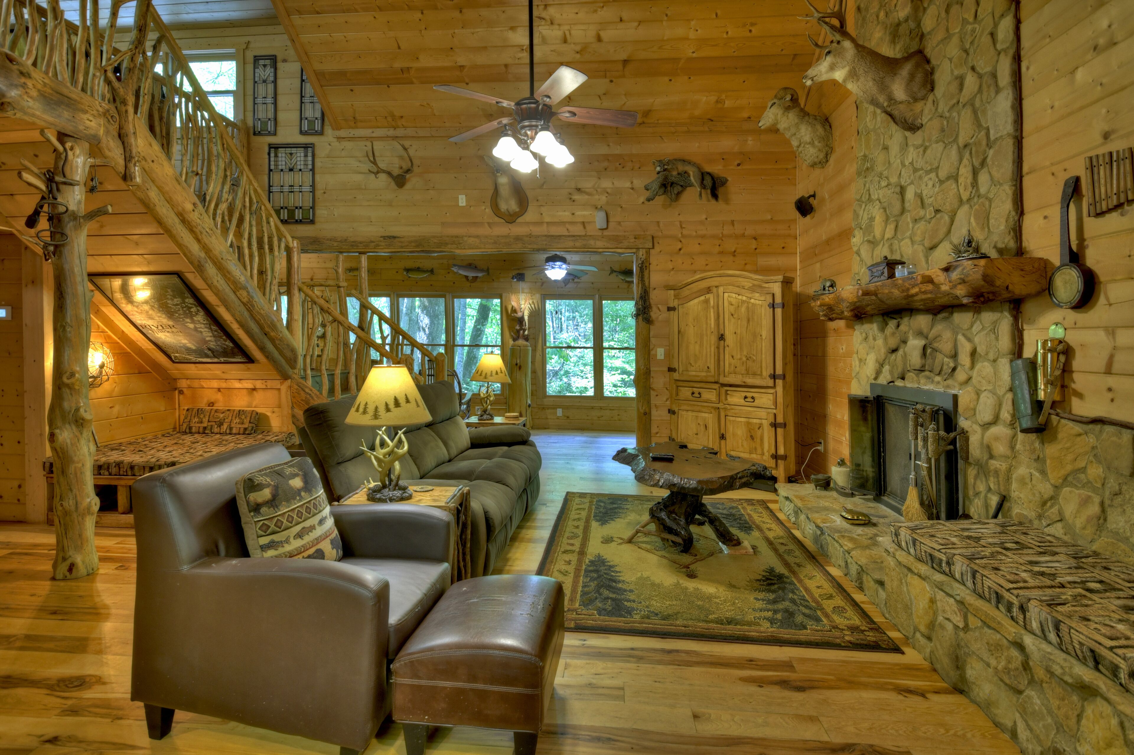 A log cabin interior with a fireplace, leather furniture, a stone wall, and a staircase.