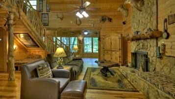 A log cabin interior with a fireplace, leather furniture, a stone wall, and a staircase.