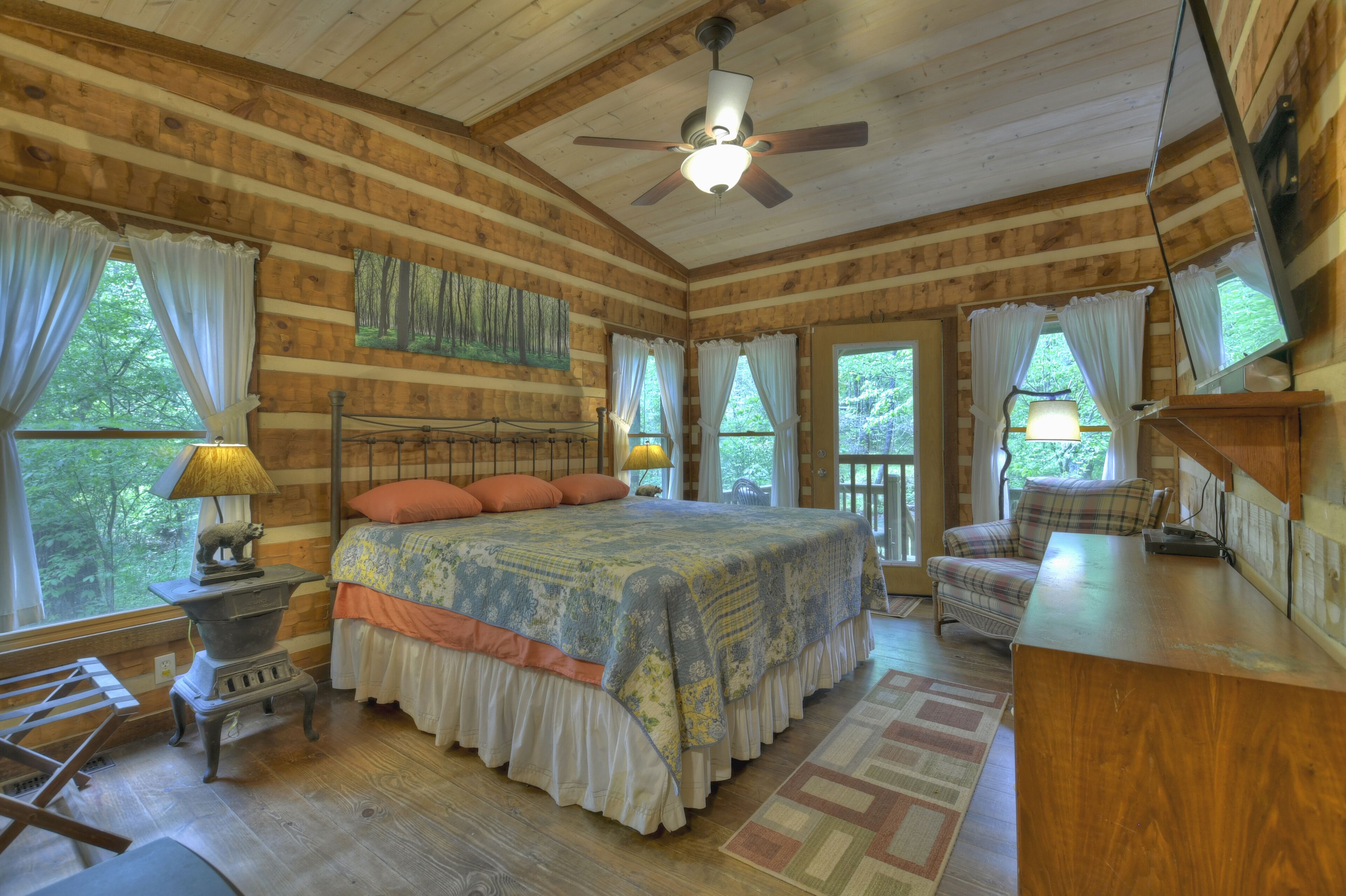 A log cabin bedroom with a large bed, a ceiling fan, and a view of the outdoors.