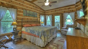 Une chambre située dans une cabane en rondins, avec un grand lit, un ventilateur de plafond et une vue sur l’extérieur.