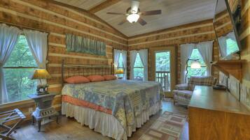 A log cabin bedroom with a large bed, a ceiling fan, and a view of the outdoors.