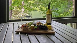 Una mesa de madera con una botella de vino, copas, y una tabla de quesos con frutas y frutos secos.