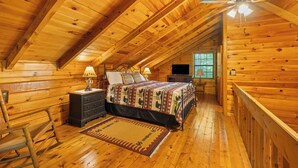 Un dormitorio de cabaña de madera con cama, cómoda, mesita de noche, lámpara y ventilador de techo.