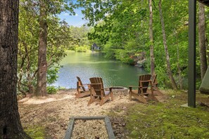 Un espace de détente aménagé au bord du lac, avec des fauteuils Adirondack et un foyer, entouré d’arbres et offrant une vue sur le lac.
