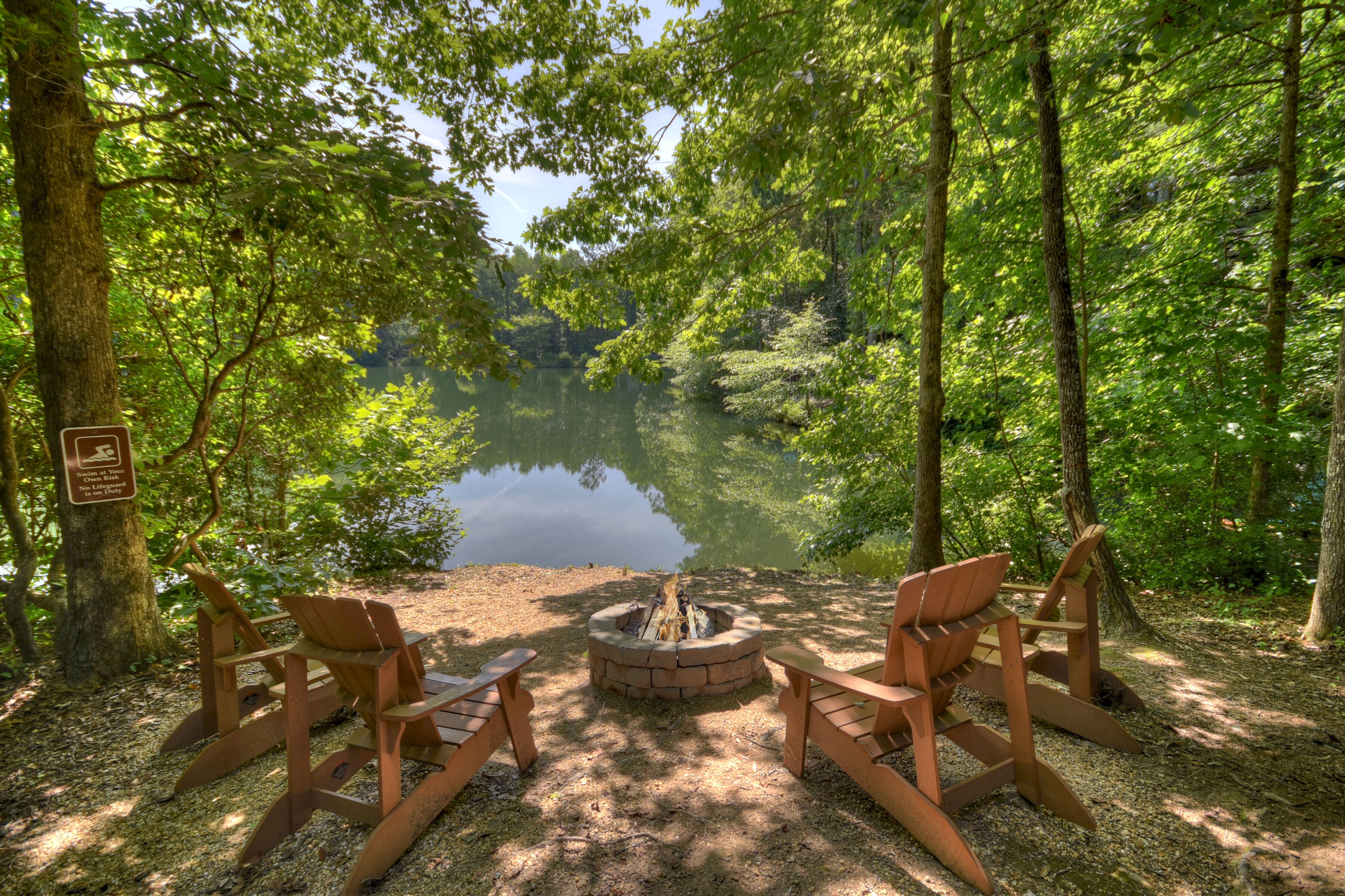 Ein Campingplatz mit Feuerstelle und Adirondack-Stühlen an einem von Bäumen gesäumten See.