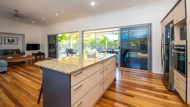 Uma cozinha moderna com uma ilha grande, sala de jantar com vista para o exterior e sala de estar com sofá e televisão.