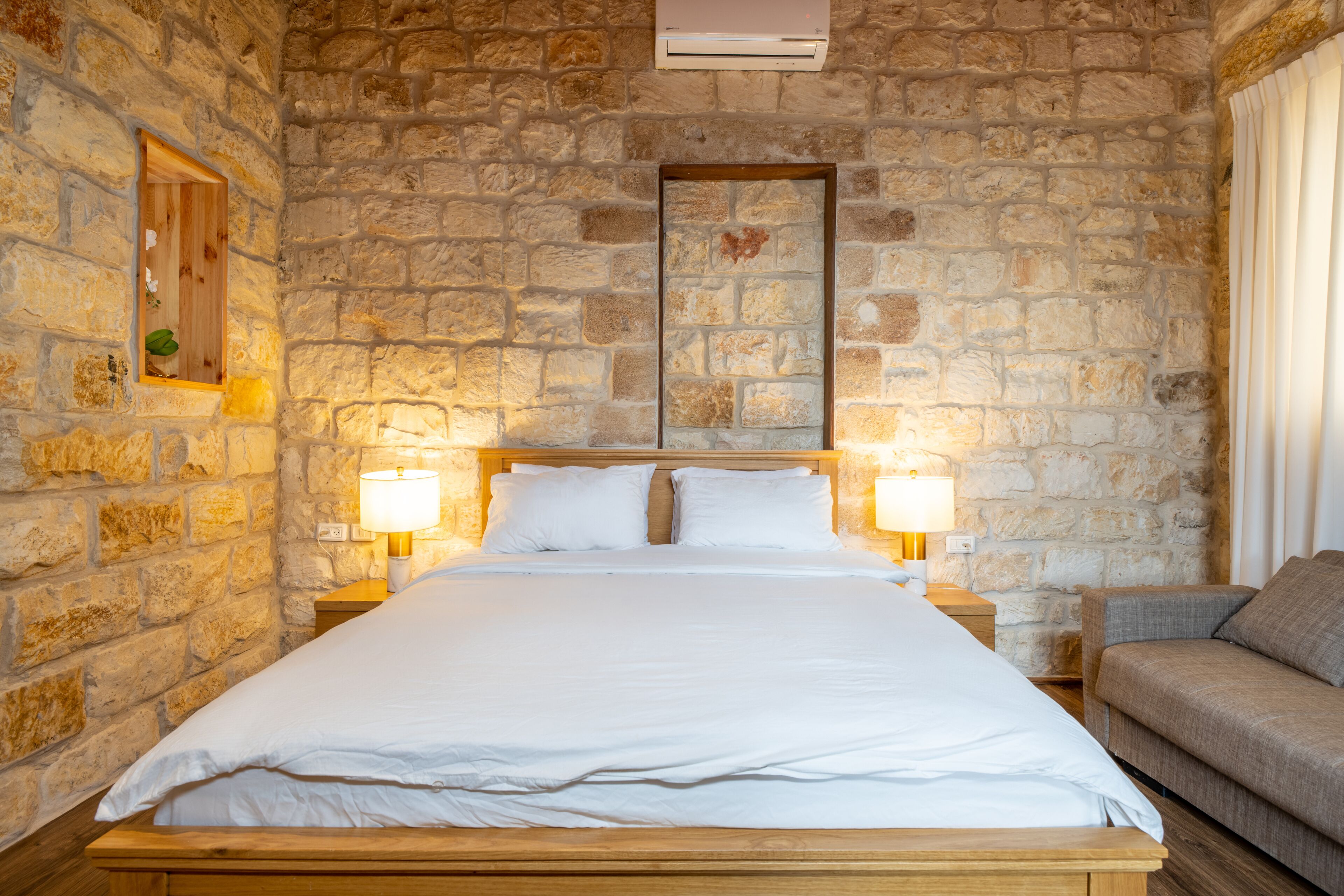 A bedroom with a stone wall, a wooden bed, two bedside lamps, and a sofa.