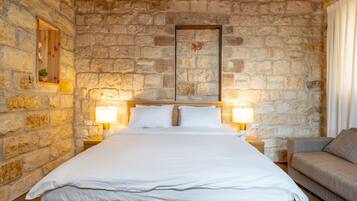 A bedroom with a stone wall, a wooden bed, two bedside lamps, and a sofa.