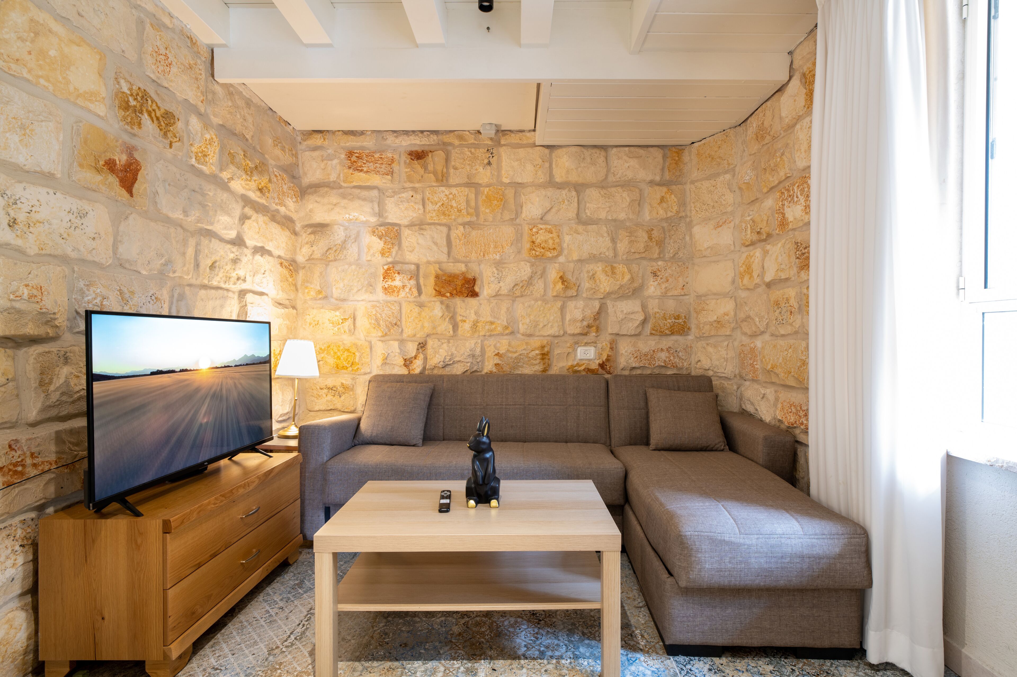 Un salón acogedor con pared de piedra, un televisor de pantalla plana, una mesa de centro de madera, un sofá y una lámpara.