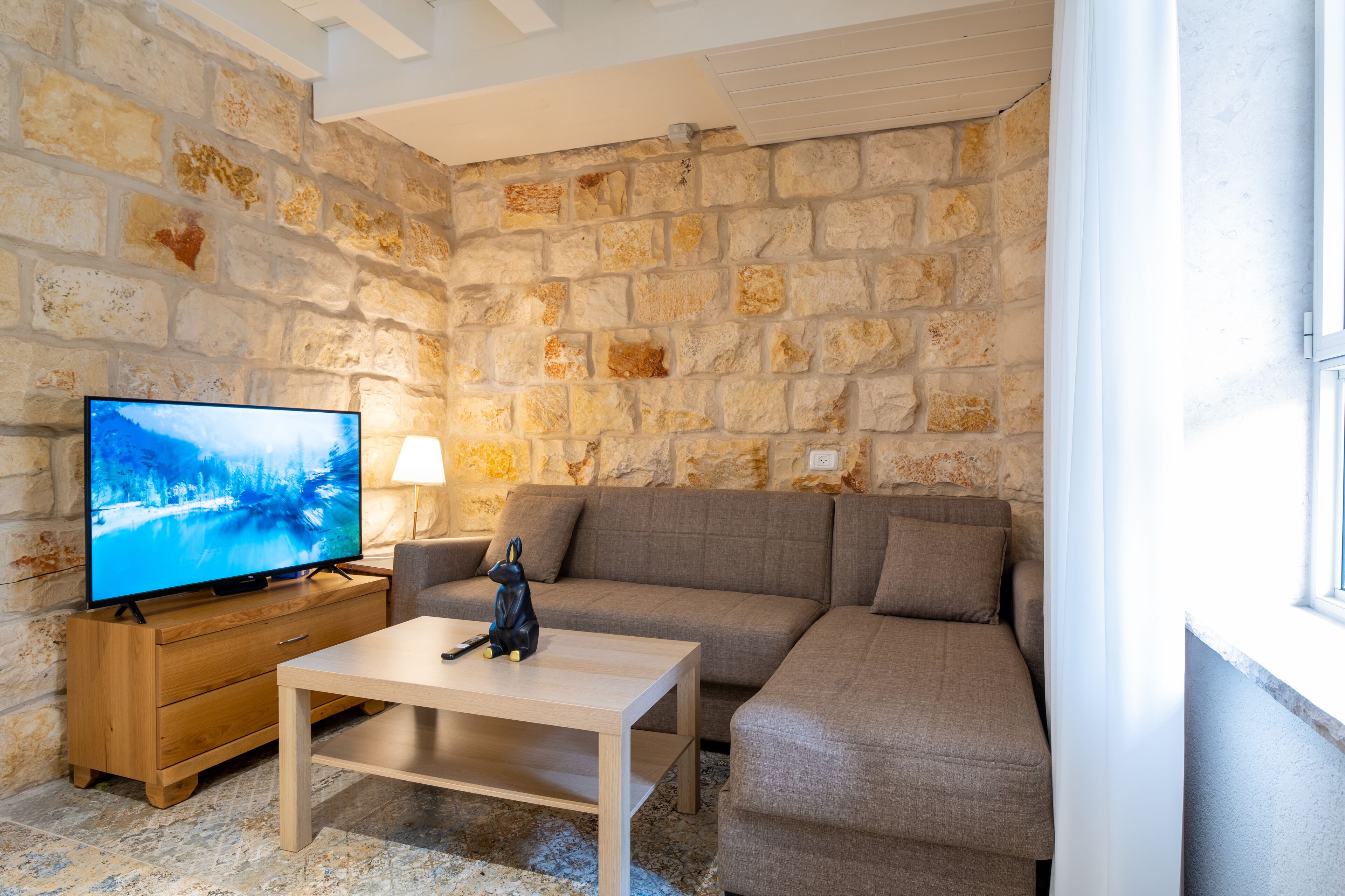 A living room with a stone wall, a television, a sofa, a coffee table, and a lamp.