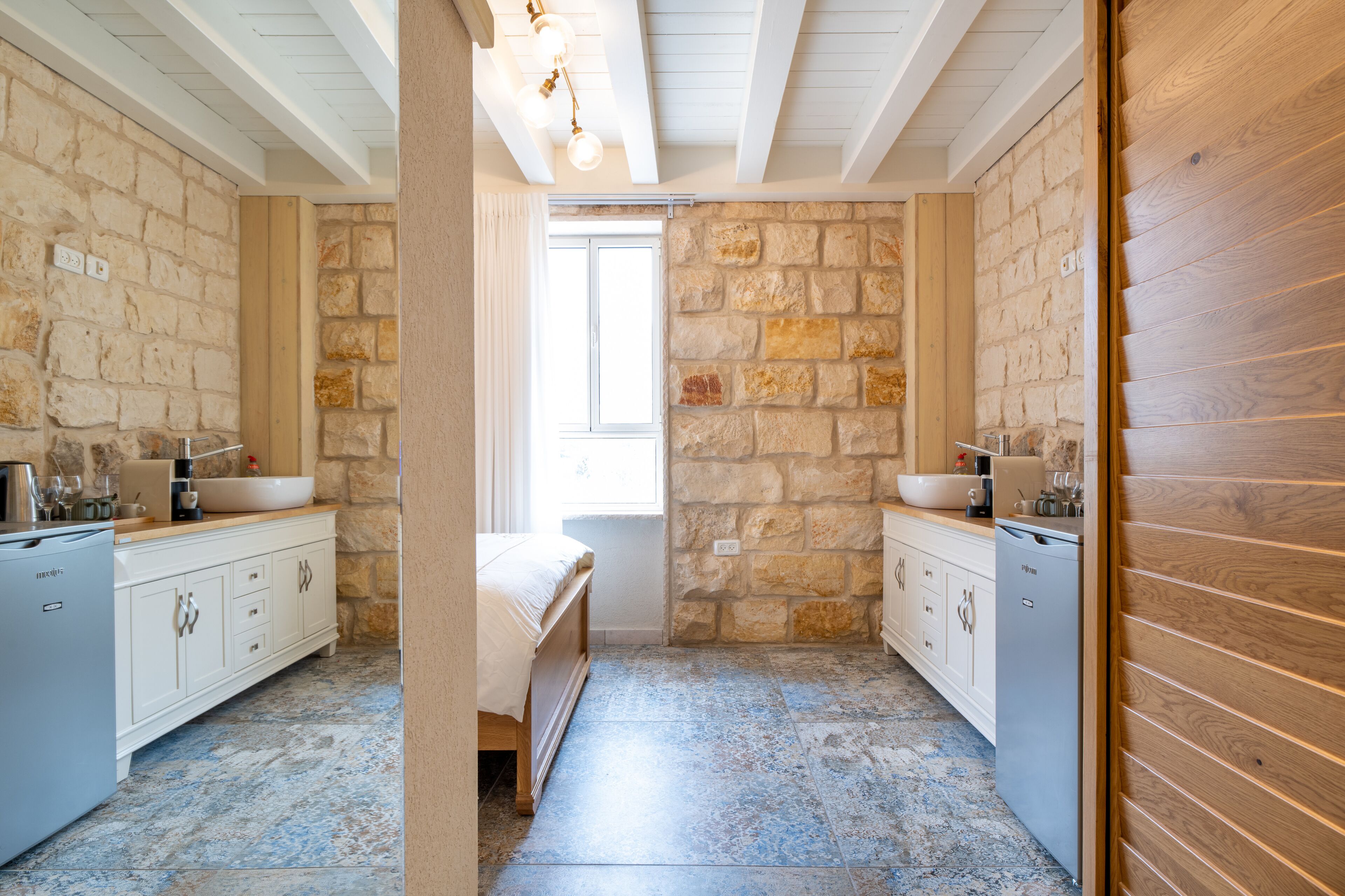 A bathroom with stone walls, a wooden vanity, a sink, and a shower area.