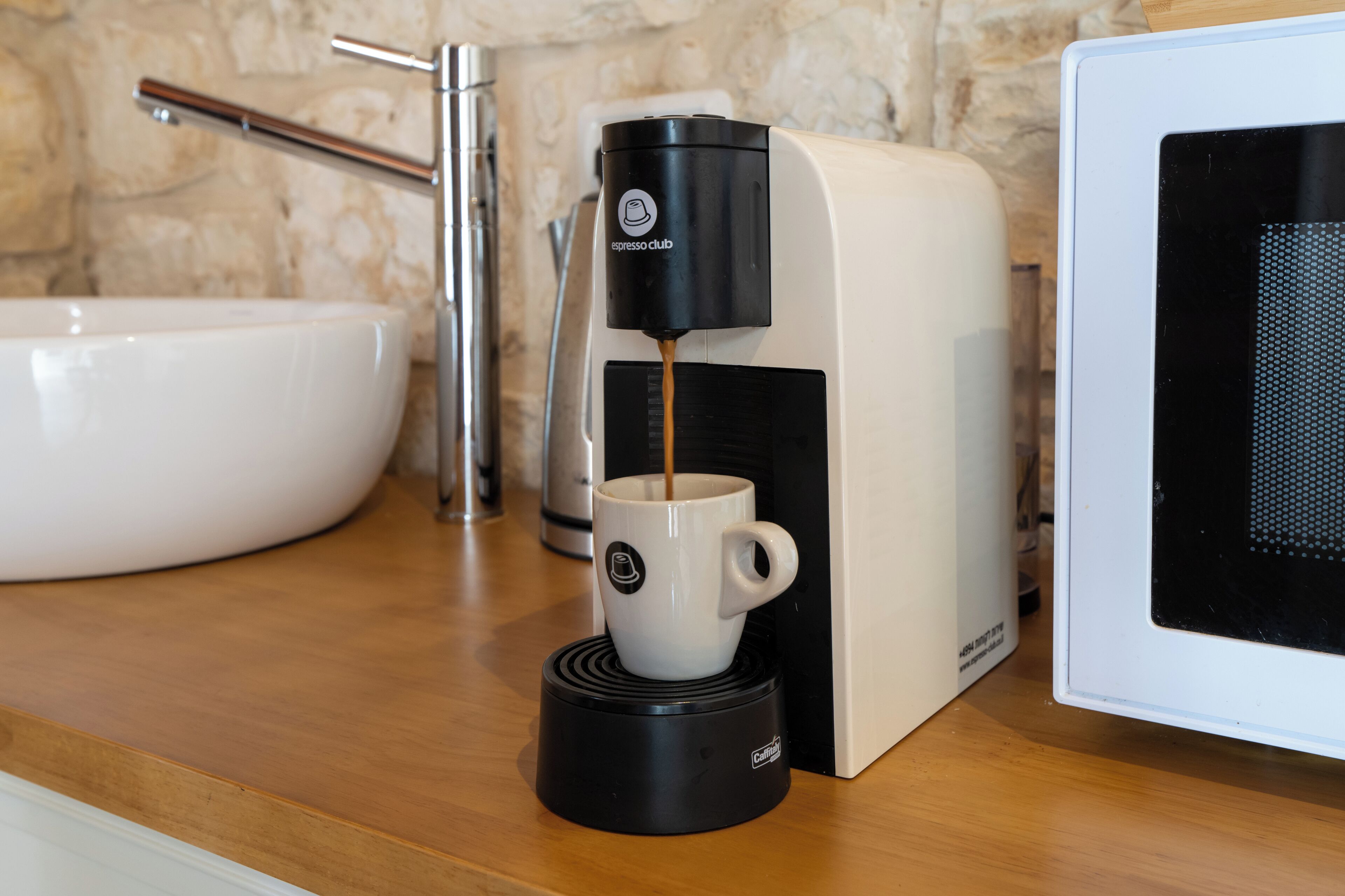 Une machine à café en train de préparer une tasse de café, un évier et un four à micro-ondes.