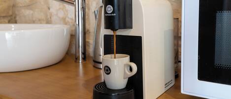 Une machine à café en train de préparer une tasse de café, un évier et un four à micro-ondes.