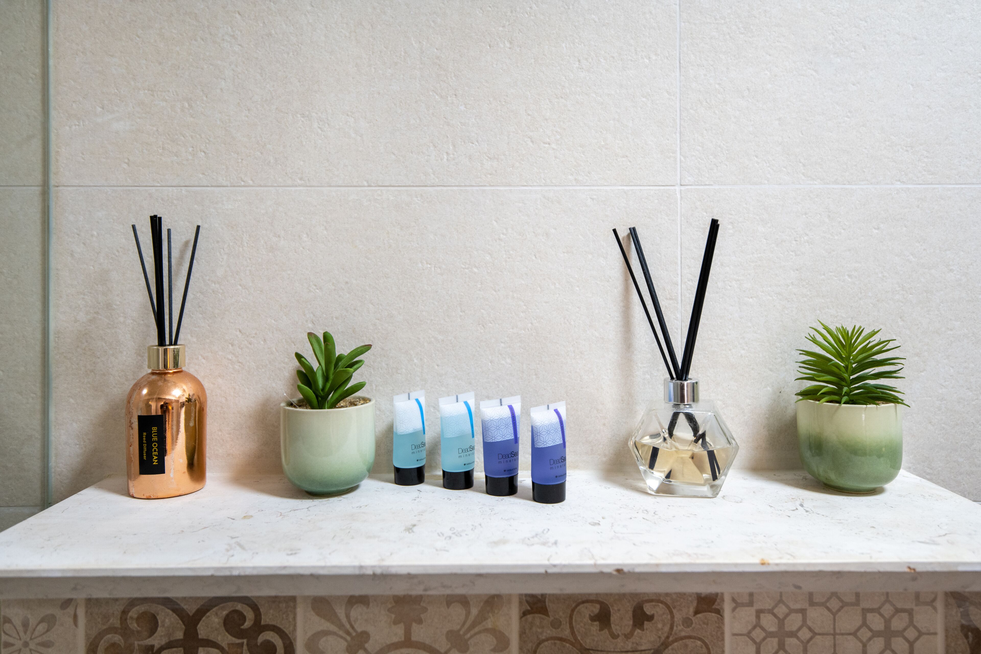 En hylla i badrummet med olika toalettartiklar, inklusive en flaska parfym, flera flaskor lotion och två krukväxter.