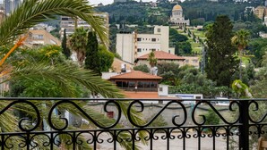 A balcony with wooden chairs and tables, overlooking a cityscape with buildings and greenery. - Via Maria Boutique Suites (Haifa)