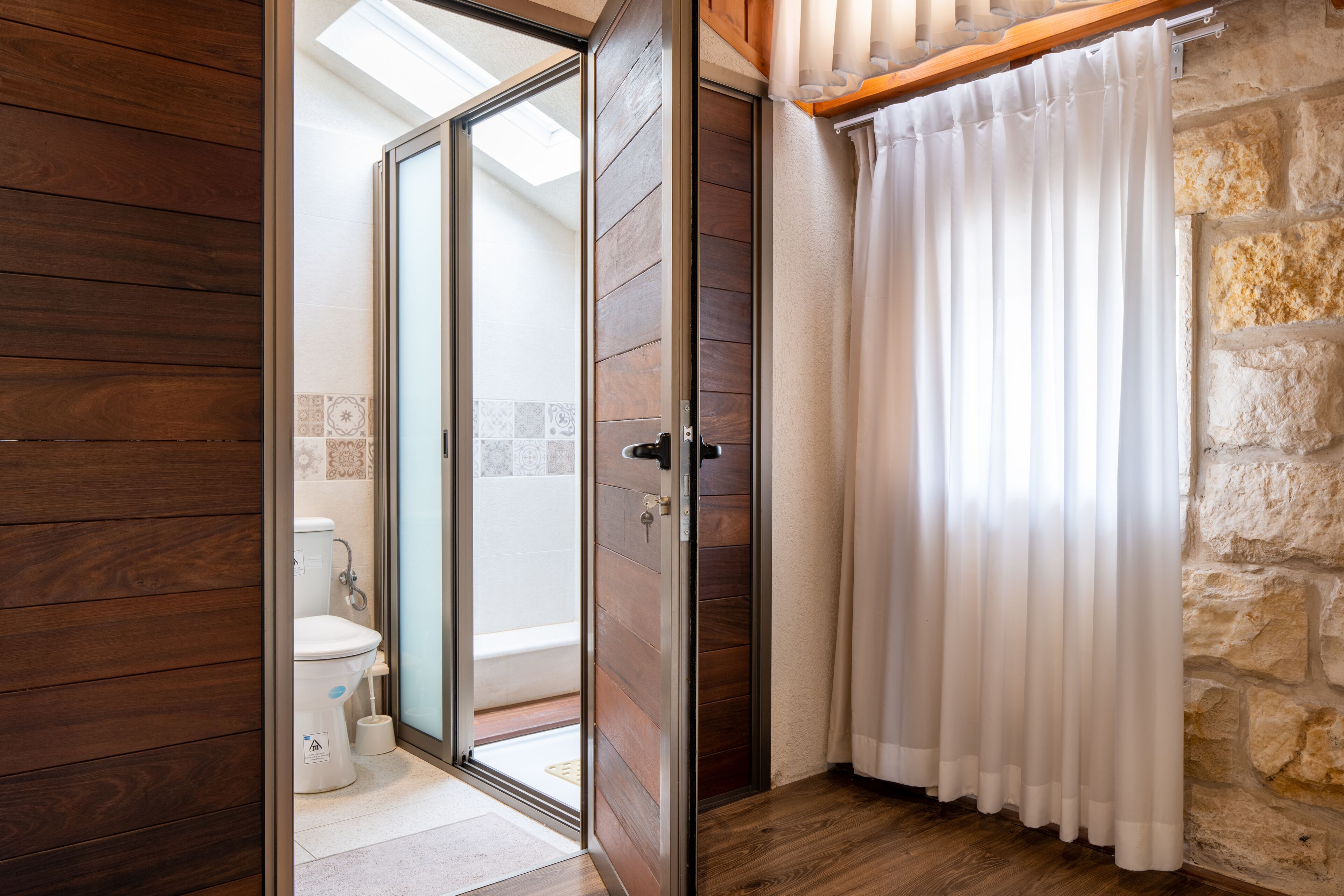 A bathroom with a wooden floor, a toilet, and a shower area with a stone wall.