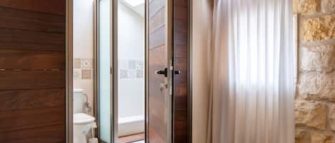 Un baño con piso de madera, un inodoro y una zona de ducha con pared de piedra.