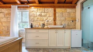 A rustic kitchen with stone walls, a wooden ceiling, a sink, and a small refrigerator.