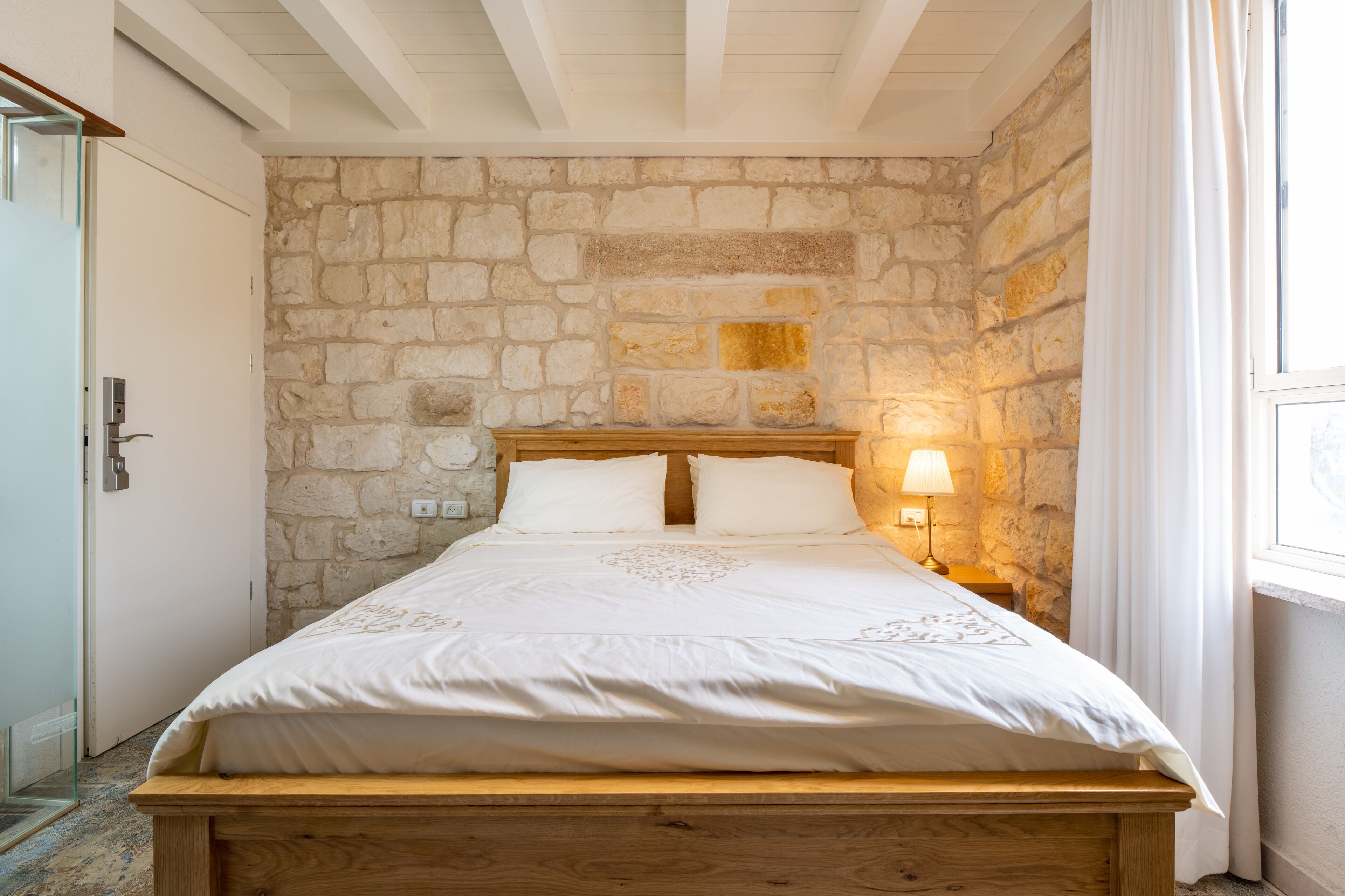 Un dormitorio con pared de piedra, estructura de cama de madera y mesita de noche con lámpara.