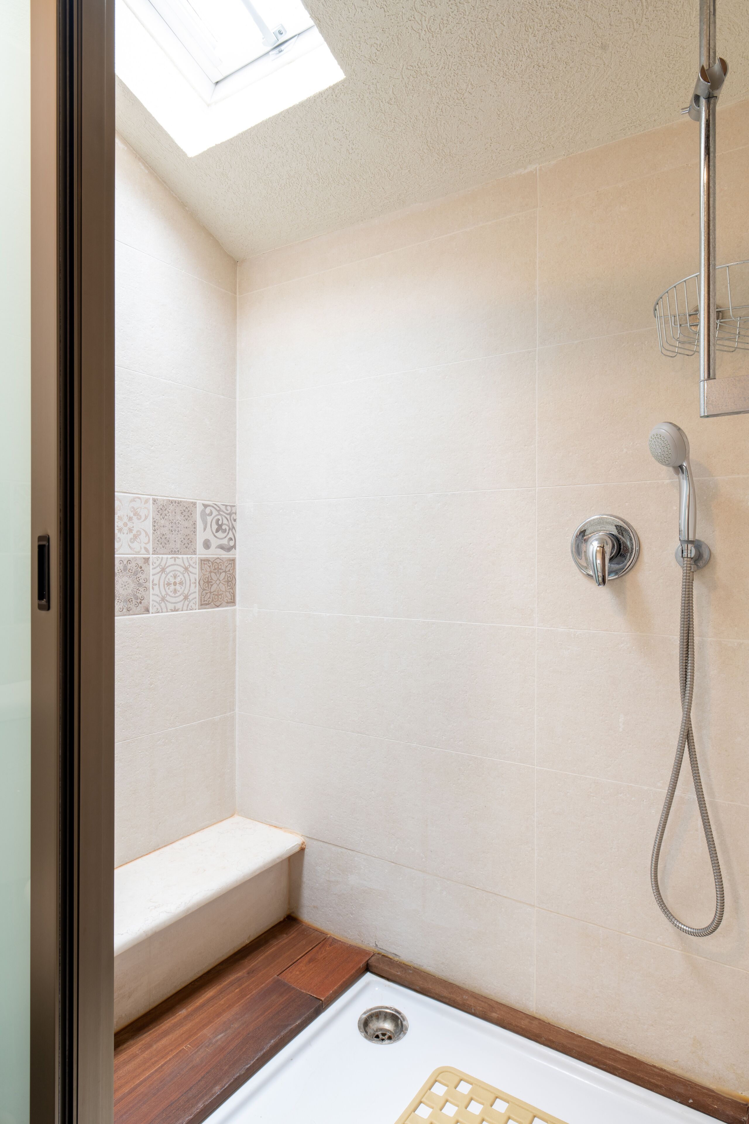 Ein kleines, modernes Badezimmer mit Dusche, Sitzbank und Oberlicht.