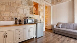 A kitchen with a stone wall, a white sink, a microwave, and a grey sofa. - Via Maria Boutique Suites (Haifa)
