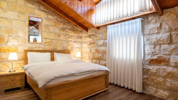 Una camera da letto con parete in pietra, soffitto in legno e un letto con biancheria bianca.