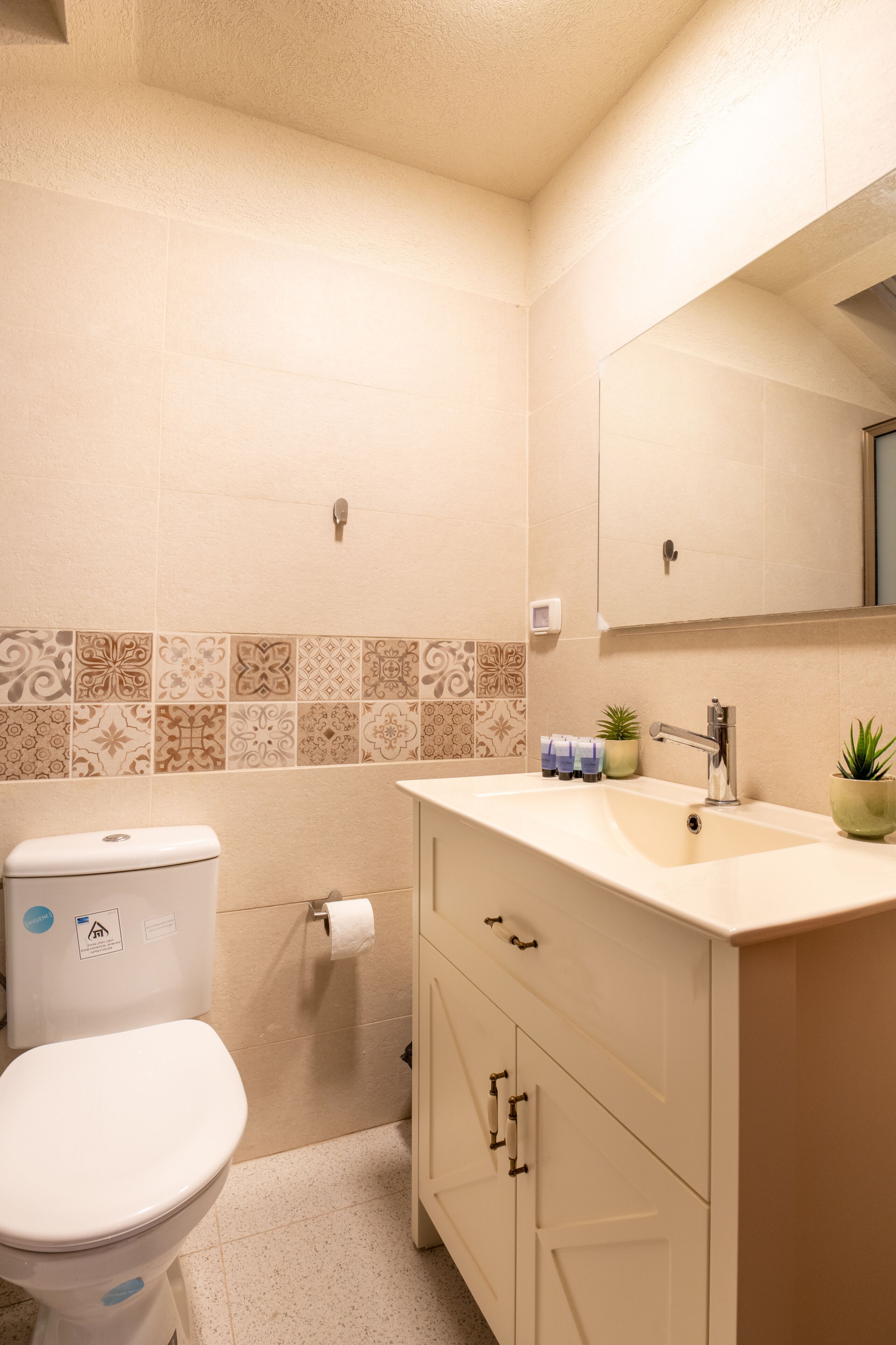 A bathroom with a toilet, sink, mirror, and decorative tiles.