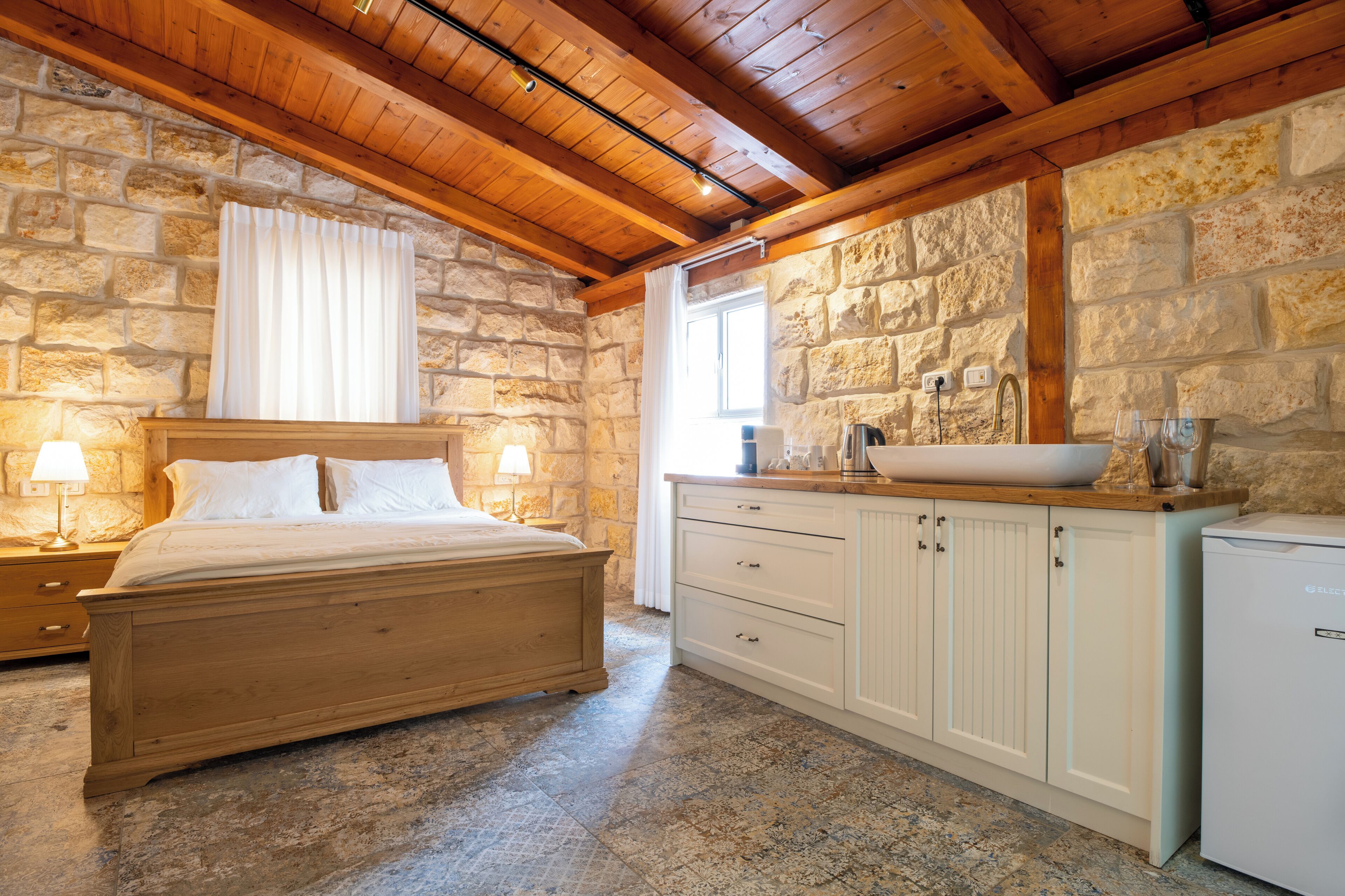 A bedroom with a wooden bed, stone walls, a stone fireplace, and a white sink.