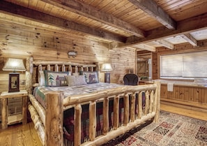 Une chambre dans un chalet en rondins, avec un lit en bois, deux lampes de chevet, un tapis à motifs et une tête de lit en bois.