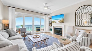 A spacious living room with a large window, a ceiling fan, a fireplace, and a TV. - Adagio B-204 Beach Front - Beautiful Gulf Front Unit! (Santa Rosa Beach)