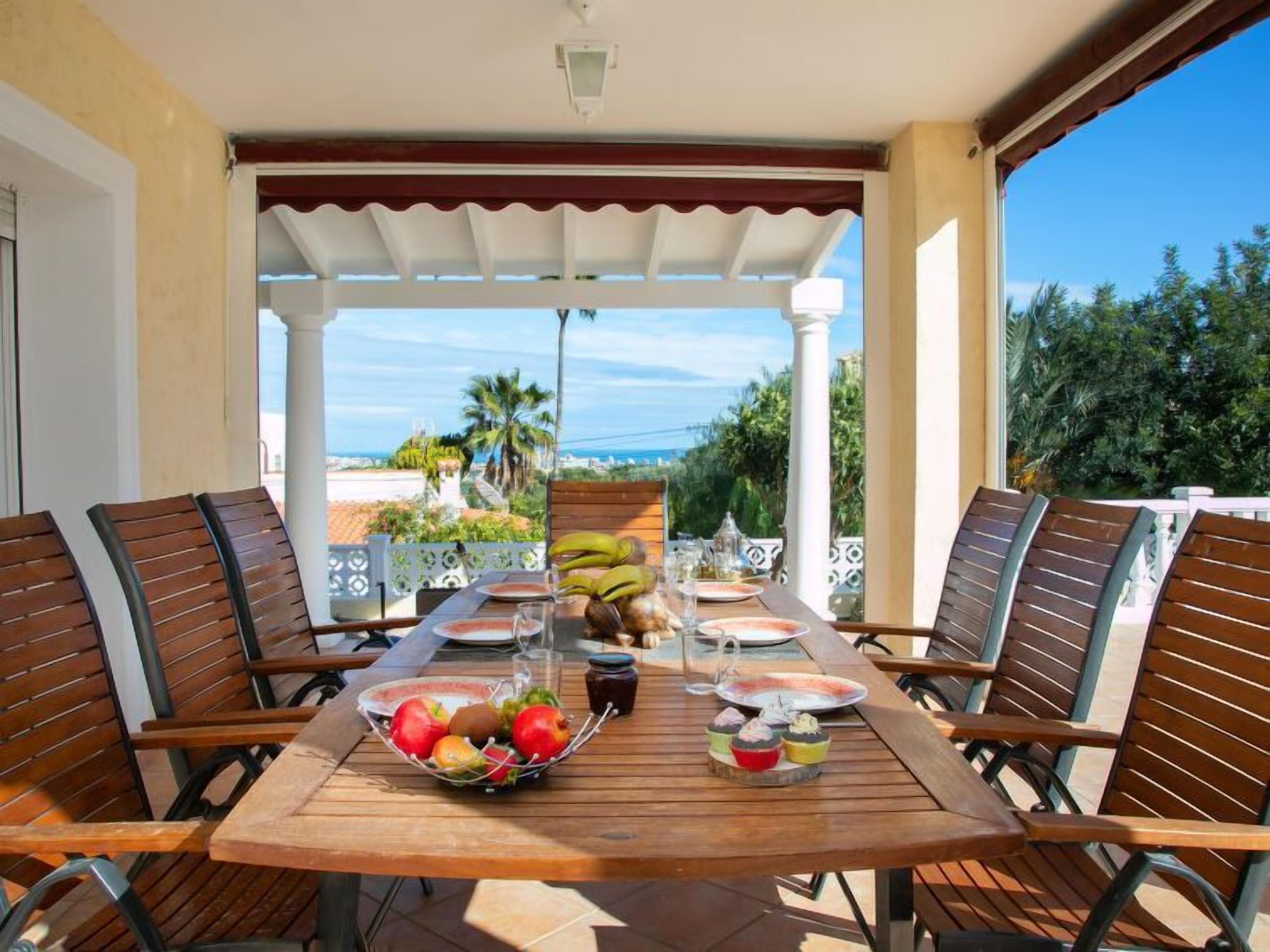 A wooden table set for four with a fruit bowl, a glass of water, and a plate of food.