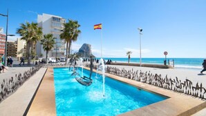 A swimming pool with a fountain, surrounded by palm trees and a flag.