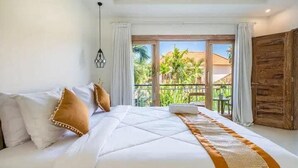 Un dormitorio con una cama grande, ropa de cama blanca y vistas a un balcón con palmeras.