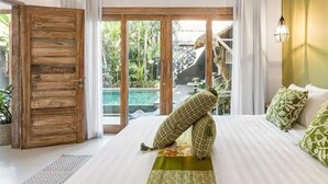 Un dormitorio con una cama grande, una puerta de madera y vistas a una piscina y vegetación exterior.