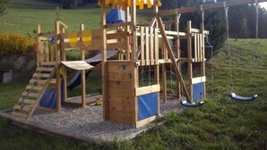 Una estructura de juego de madera con tobogán, pared de escalada y columpios.