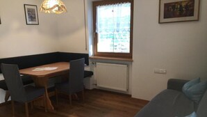 Un espacio habitable pequeño con una mesa de madera, dos sillas, un sofá gris y una ventana que da a zonas verdes.