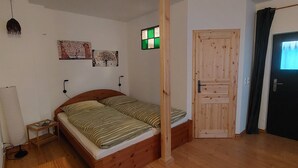 Un dormitorio con cama de madera, una mesita de noche pequeña, una lámpara de pared y una puerta con panel de madera.